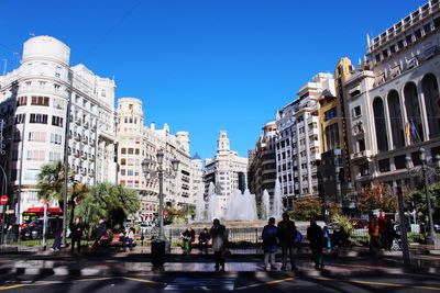 People on street in city against clear blue sky