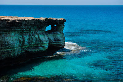 Rock formation on sea shore against blue sky