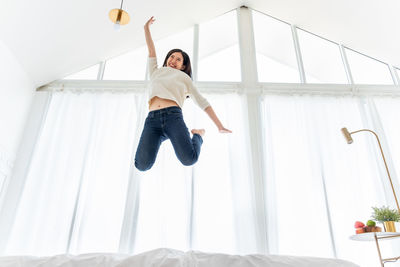 Low angle view of young man jumping on bed at home