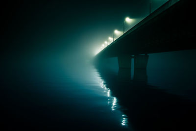 Low angle view of illuminated bridge over river at night