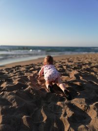 Girl crawling on sand against clear sky