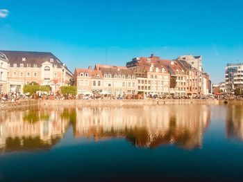 Reflection of buildings in lake against blue sky