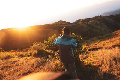 Rear view of man standing on mountain against sky during sunrise