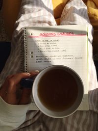 Midsection of woman holding hot drink on spiral notebook