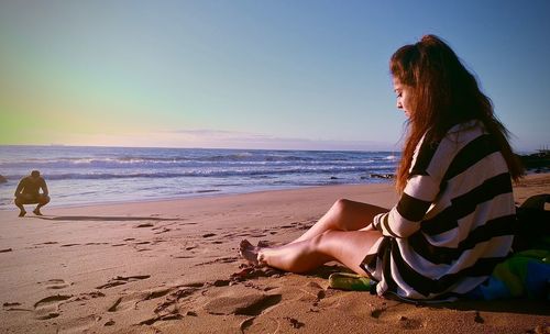 Woman sitting on shore at beach against sky