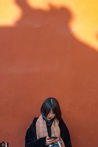 Portrait of woman standing against orange wall