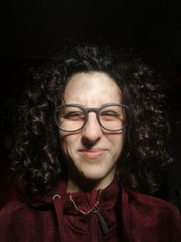 Close-up portrait of smiling woman with curly hair against black background