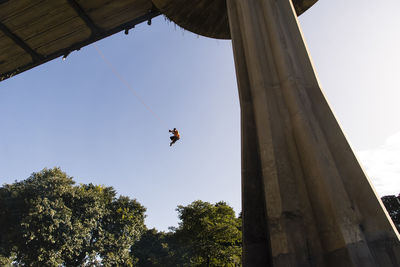 Low angle view of man rappelling against clear sky
