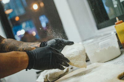 Gloved hands of man working with pizza dough in kitchen