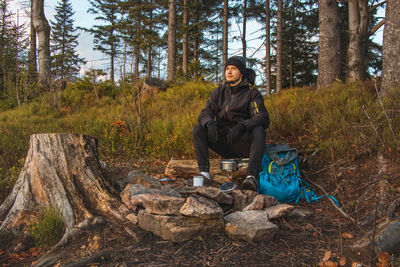 Outdoor wilderness trekking enthusiast sitting by a campfire enjoying breakfast at sunrise