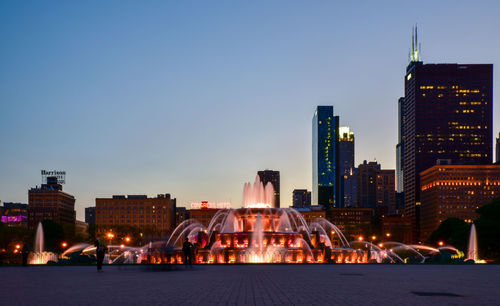 Illuminated buckingham fountain against skyscrapers in city at dusk