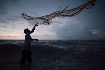 Fisherman throwing net in sea against sky