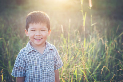 Portrait of happy boy standing on grassy field during sunny day