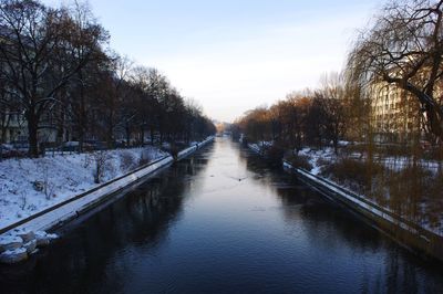 Canal amidst trees against sky during winter