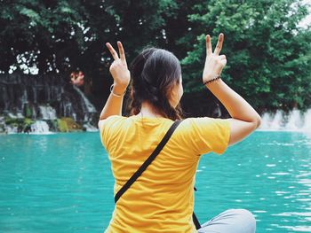 Rear view of woman gesturing peace sign while sitting by swimming pool