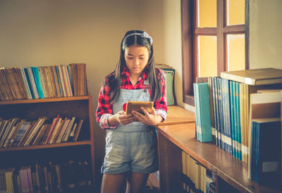Girl using digital tablet while standing in library