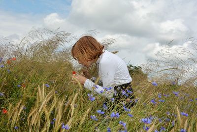 Rear view of woman standing by flowering plants on field against sky