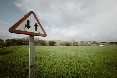 Road sign on field against sky