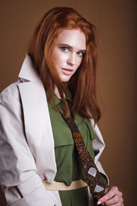 Portrait of young woman standing against brown background