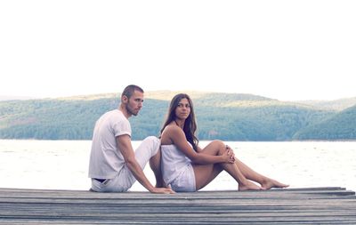 Young couple sitting on pier against lake