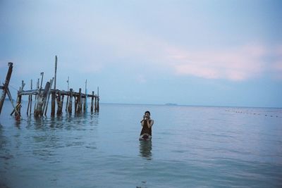 Woman standing in sea against sky during sunset