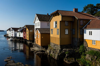 Buildings by river against clear blue sky