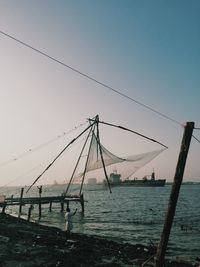 Silhouette fishing net on shore against clear sky