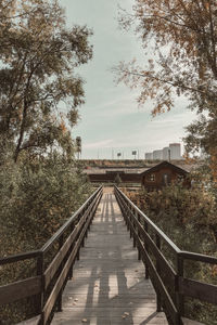 Footbridge amidst trees and building against sky