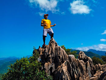 Low angle view of man standing on rock against sky