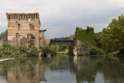 Old fortress by lake against cloudy sky at valeggio sul mincio