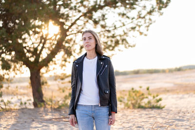 Woman wearing jacket standing at beach during sunset