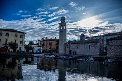 Buildings at waterfront against cloudy sky