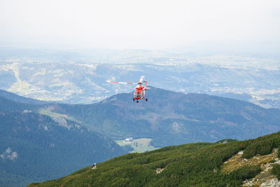 Helicopter flying over mountains against sky