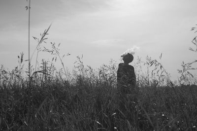 Young woman smoking on field against sky