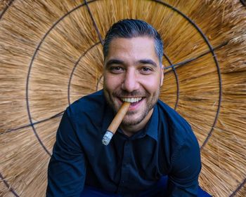 Portrait of smiling young man smoking cigar against thatched roof