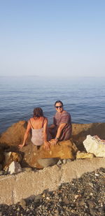 Man sitting on rock at sea shore against clear sky