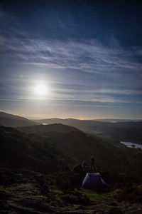 Distant view of people by tent on mountain against sky during sunset