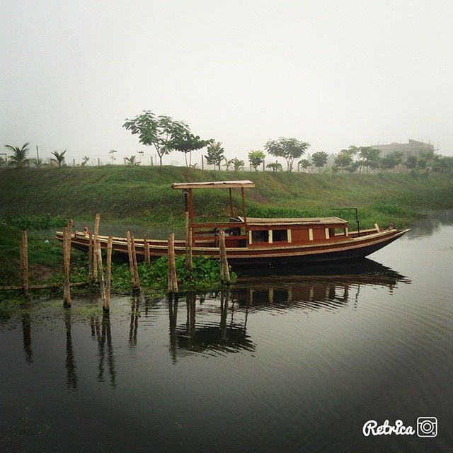 water, lake, clear sky, tranquil scene, tranquility, reflection, tree, waterfront, nature, copy space, scenics, beauty in nature, river, day, pier, built structure, grass, outdoors, green color, nautical vessel