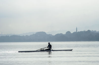 Man rowing boat in sea against sky