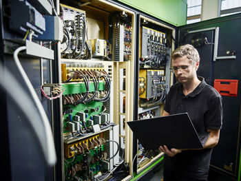 Technician using laptop at machine in modern factory