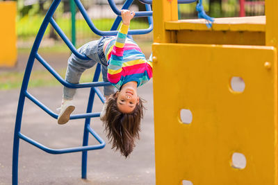 Funny little smiling girl 5-6 years old, hanging upside down  at the playground