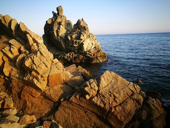 Rock formation in sea against clear sky