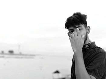 Portrait of young man standing at beach against sky