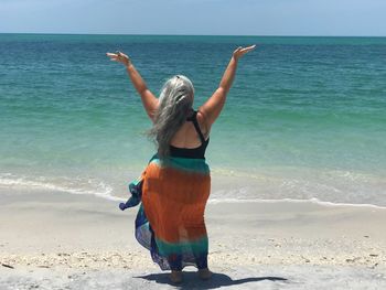 Rear view full length of woman with arms raised standing on shore at beach