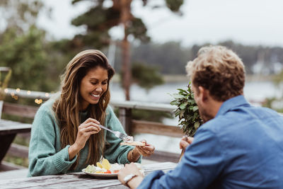 Smiling woman eating food while sitting with male friend in restaurant