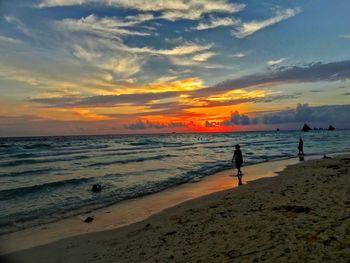 Silhouette people walking at beach against sky during sunset