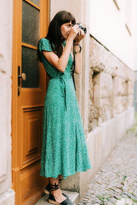 Young woman photographing while standing against wall