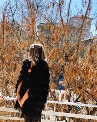 Rear view of woman standing amidst plants during winter