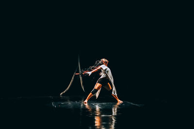 Young woman dancing against black background