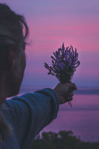 Close-up of man holding plant against sky during sunset